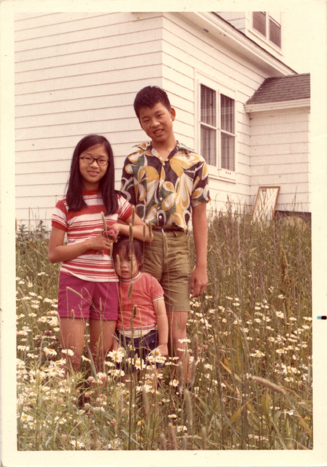 A small child and adults in a flower garden in front of a white house at 110 Granville Street, Port Hawkesbury, 1972